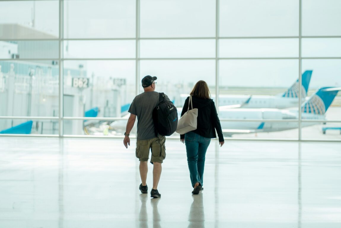 Two travelers with bags walking through a bright airport terminal